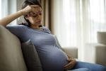 Tired stressed pregnant woman sitting on a couch. Visual concept for a employee attorney blog discussing your possible legal rights if you are pregnant and laid off.